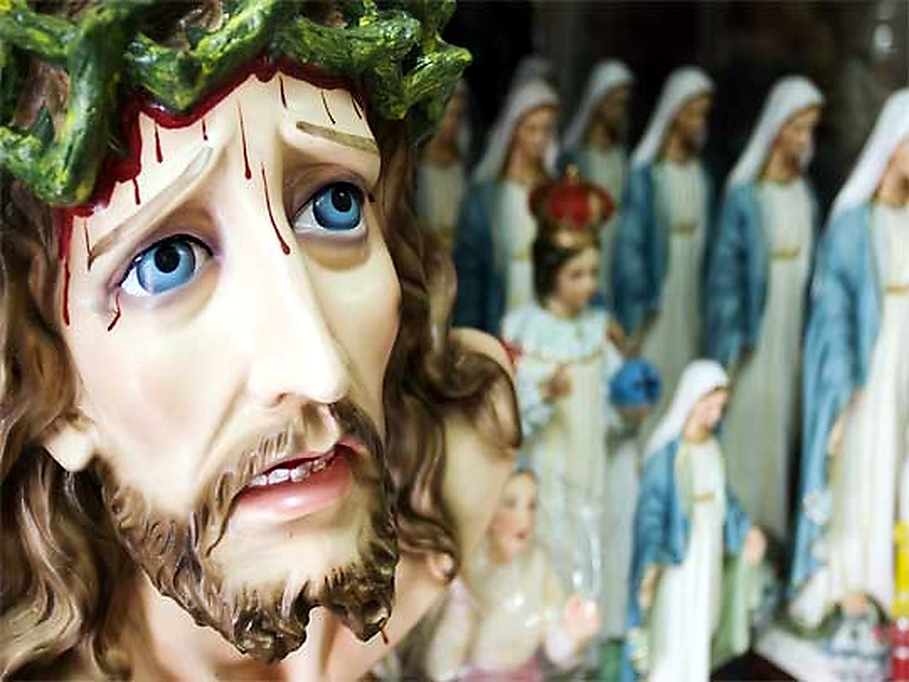 Фигурка Христа в терновом венце крупным планом Расписная статуя Христа в терновом венце рядом с другими религиозными фигурками